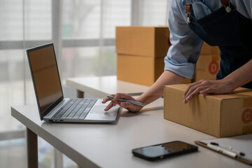 Online seller preparing cardboard box for delivery and using laptop