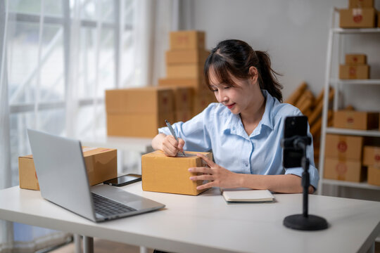 Young asian woman entrepreneur writing address on cardboard box preparing for delivery
