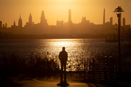 Person standing looking at waterfront city skyline during sunset - Powered by Adobe