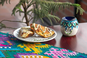 Photograph of fried empanadas with sauce on a white plate with a colorful tablecloth on a table