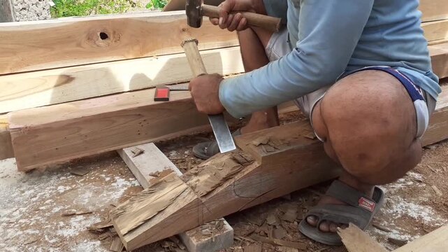 a construction worker carves wood to build a house with a chisel