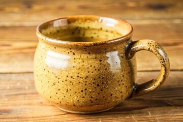 Handmade speckled golden brown ceramic mug with a rustic glaze on a wooden table