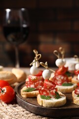 Delicious bruschettas with salami, mozzarella and tomatoes served with red wine on table, closeup