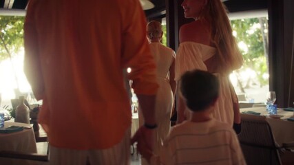 Family walks into a restaurant in a tropical setting. Shows the anticipation and connection of shared moments and the essence of relaxed luxury, togetherness, and memorable dining while on vacation.