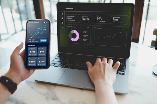 A financial analyst multitasking, checking an investment portfolio on a smartphone and a business data dashboard on a laptop.