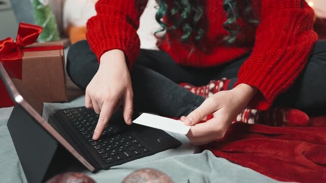 Close up hands womans using tablet and holding credit card during Christmas shopping at home, ordering gifts online in cozy festive interior with warm lights
