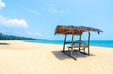 Cottages made from natural materials are located along a stretch of beach lined with pine trees during the daytime.