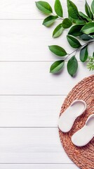 A top-down view of white flip-flops on a woven mat, with green leaves and a white wooden background.