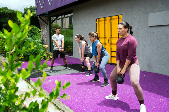 Latin american fitness enthusiasts performing kettlebell squats during an intense outdoor workout session, building strength and health