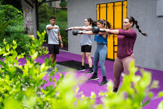 Latin american women working out with kettlebells outdoors, receiving guidance from a male personal trainer in a modern fitness center