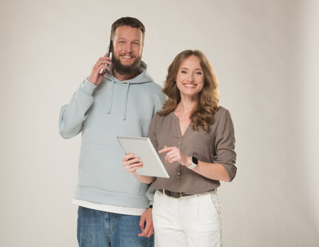 A young, joyful man and woman with a tablet and smartphone approve, promote, and recommend. A couple of young people with electronic devices in casual, muted clothing look at the camera with positive 