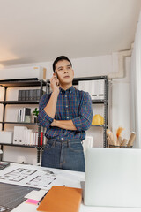 Confident young architect working at office desk, drawing house plans and discussing construction details on the phone, focusing on accuracy and creativity in architectural design and project planning