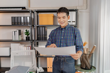 A young architect works with building plans and a house model in the office, reviewing blueprints, marking details, and analyzing design structures with focus and creativity.