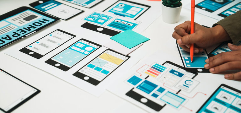A person sketches a digital interface on paper mockups using colorful stationery, showcasing the creative process in user experience design and innovative ideas. SACTR