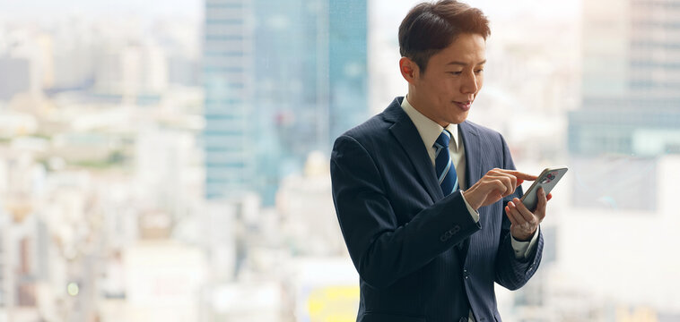 都市を背景にスマホを使う男性ビジネスパーソン