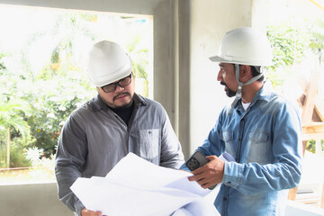 Two construction workers, architect, engineer, contractors clad in safety helmets and glasses, engage solving problem discussion and pointing roof or ceiling of the construction site, safety planning
