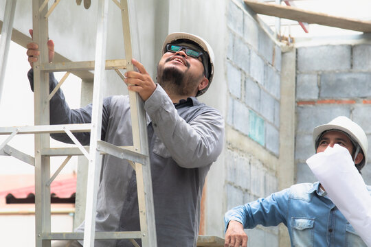 Young overweight engineering foreman climbing ladder inspect ceiling unfinished building or fixing error man work at construction site outdoors with Asian or Indian contractor man business partnership