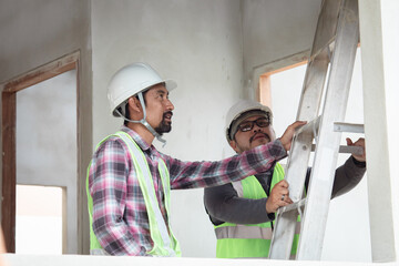 Asian or Indian contractor man business partnership inspect ceiling room mistake labor working error climbing ladder using measurement equipment with young foreman worker wearing safety white helmet © Rakchanok