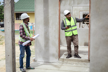 Two construction foreman workers examine inspect unfinished property site outdoor, Asian or Indian contractor man partnership and engineering project manager wearing reflection vest working together