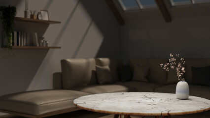 Flower vase on round marble table across leather sofa couch under roof window in dim attic living room.