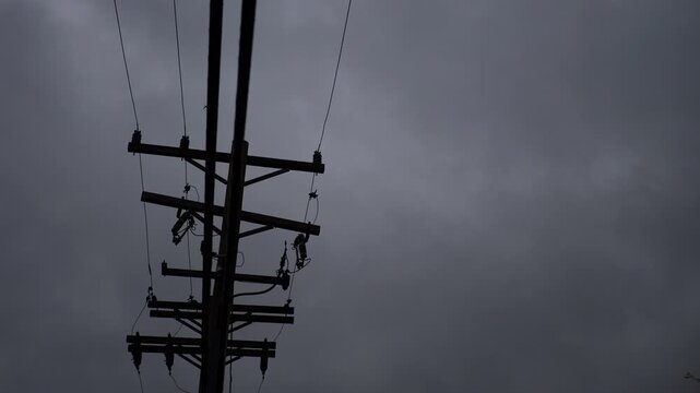 Silhouette of electric tower with power lines against a dark, foreboding sky and leaves blowing across in the wind.