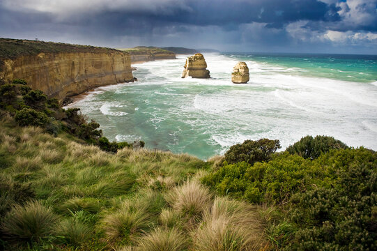 Stormy coastal view with cliffs, ocean waves, and sea stacks.
