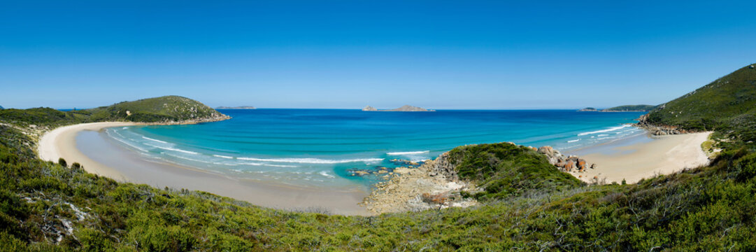 Panoramic view of a turquoise bay with twin beaches framed by green coastal hills