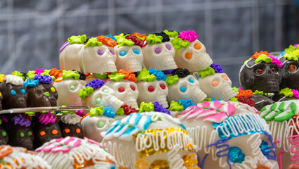 A row of decorated skulls are displayed on a table. The skulls are decorated with colorful icing. Mexican Day of the Dead tradition, offerings, food, colors, decorations, and papel picado, La Catrina.