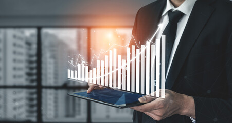 A professional businessman focuses on analyzing data trends using a digital tablet in a modern office setting, enhanced with a graphic overlay of growth indicators. Impute