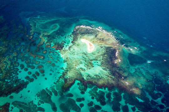 Tiny sandy cay surrounded by vivid coral reef.