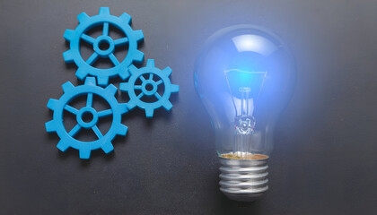 Light bulb shining over blue gear mechanism representing innovation, teamwork, and inspiration.