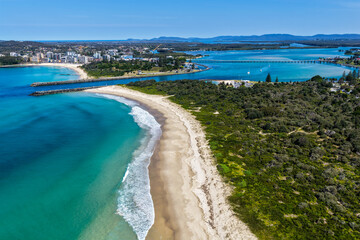A breathtaking aerial view of Forster on the Mid North Coast of New South Wales, showcasing turquoise ocean waters, white sandy beaches, and the bridge linking Forster and Tuncurry. The scenic coastli