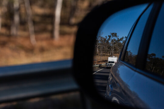 car towing caravan seen in vehicle side mirror on highway road trip