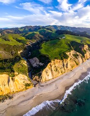 Aerial view of a beach, cliffs, rolling green hills under a blue sky