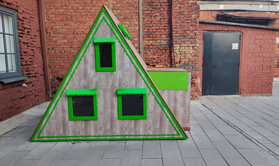 Unique triangular playhouse stands out against red brick wall in urban setting © Svetlana Verbitskaya