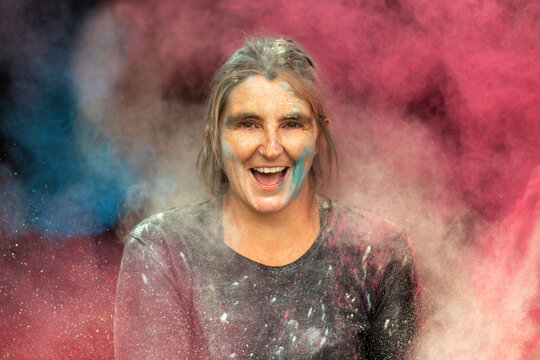 Laughing woman covered in colorful Holi powder cloud, symbol of joy, creativity and self-expression