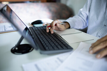 asian businessman using tablet computer working online at home with documents on desk