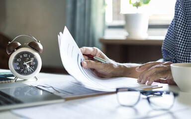 close up shot, asian retired man working at home reading document for a new job using laptop start to work online start new job after retirement