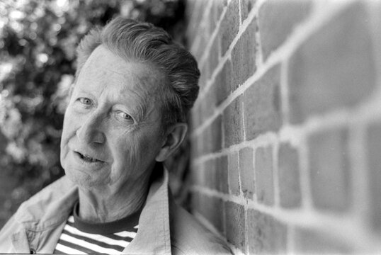 Senior man leaning against brick wall in grainy monochrome analog photo