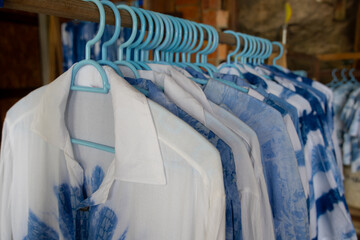 close-up shot of tie-dye t-shirts hanging on light blue plastic hangers. The shirts feature a soft, pastel tie-dye pattern.