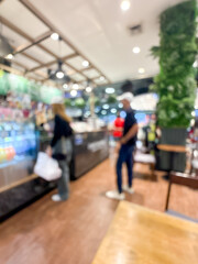 blurry image showing the interior of a shopping mall. The scene is out of focus, with indistinct shops, lights, and people walking.