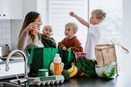Mother with young boys unpacking groceries on the countertop in the kitchen