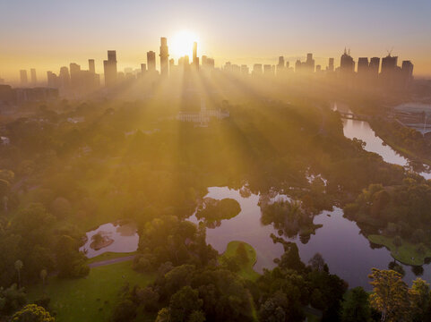 Aerial view of rays of golden sunshine between high rise buildings and over inner city parkland
