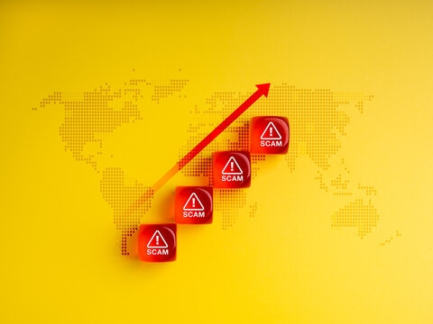 Global scam growth concept with red alert icon cubes and upward arrow on world map yellow background. Symbolizing rise of cybercrime, online fraud, and international scam threats in the digital age.