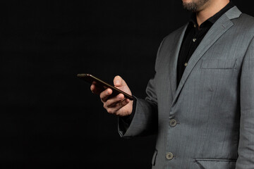 Naklejka premium a businessman at the right side of the screen watching his smartphone and a black background