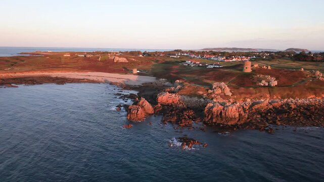 Reveal drone footage of Martello Tower on the headland at Lancresse Bay Guernsey with calm water,beach and rocks in the stunning colours of the golden hour