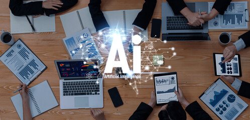 A top view of a business meeting discussing artificial intelligence, with laptops, tablets, and analytical charts spread on a wooden table, showcasing teamwork and innovation. Trope