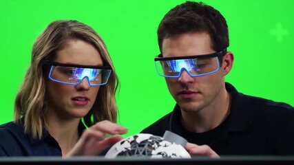 Two diverse individuals wearing futuristic augmented reality glasses interact with a holographic globe in a green screen studio representing advanced technology and virtual experiences. - Powered by Adobe