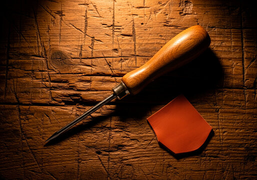 Artisan leatherworking awl — wooden handle, rustic workbench, traditional handmade craft concept