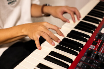 Fototapeta premium Close-up of a musician playing a red electronic keyboard indoors, showing focused hand movements across the piano keys.